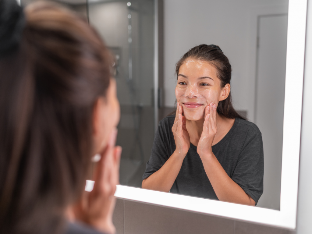 A picture of a woman exfoliating skin in front of the mirror. Skincare essentials: Exfoliation