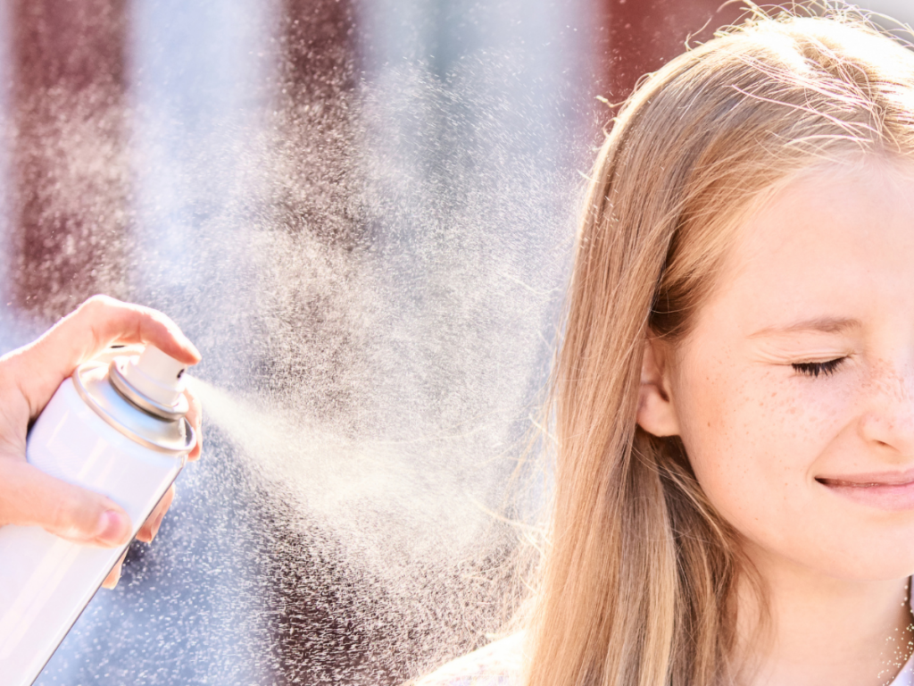A picture of a little girl having heat protectant spray applied to her hair.