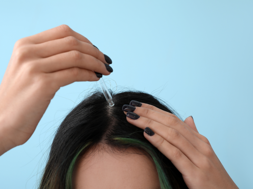 A picture of a woman applying scalp treatment to her hair.