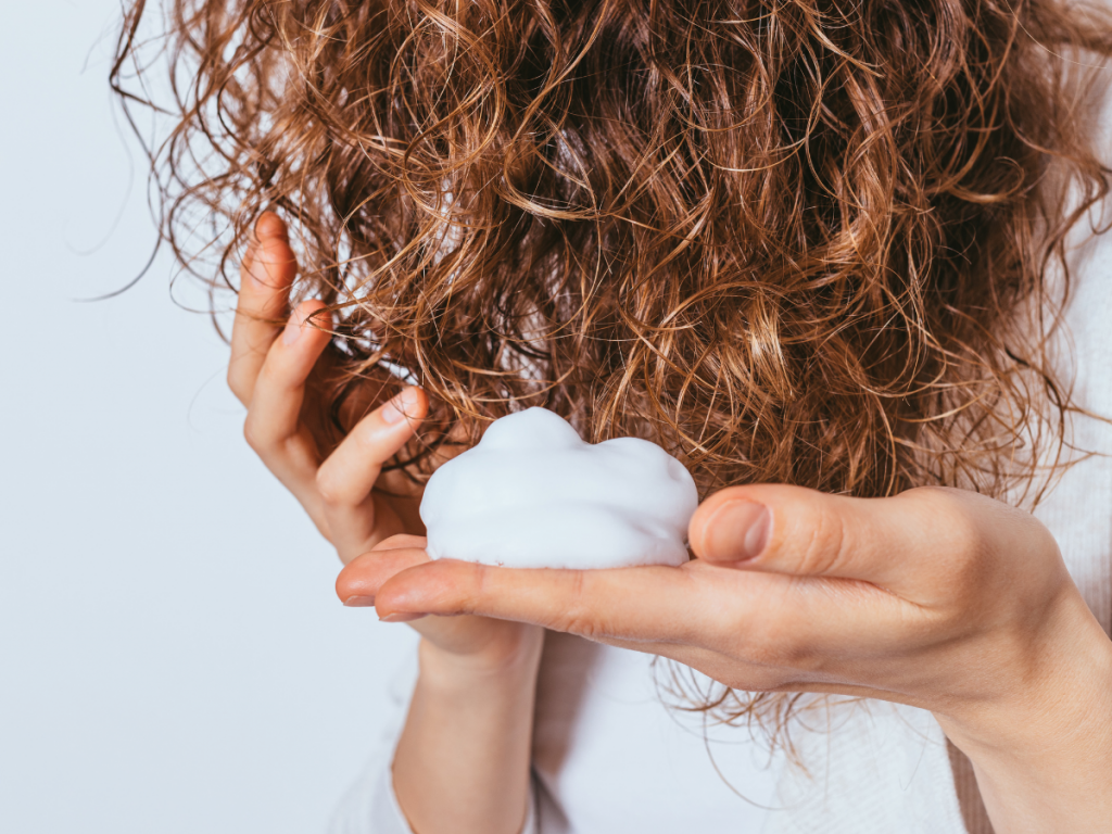 A picture of a woman holding a dollop of mousse for her hair.